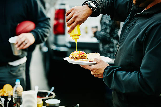 man putting mustard on burger at tailgating party - food stock pictures, royalty-free photos & images