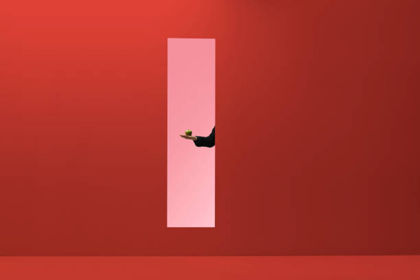 man reaching hand out threw rectangular opening in coloured wall and holding apple - food stock pictures, royalty-free photos & images