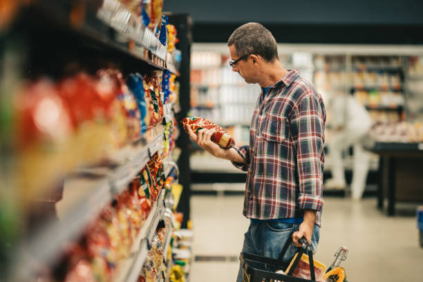 man reading a label while grocery shopping in a supermarket aisle - food stock pictures, royalty-free photos & images