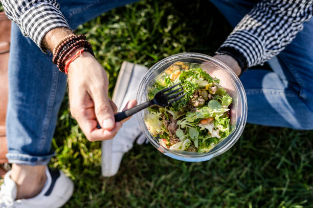 man sitting on a meadow eating mixed salad, partial view - junk food stock pictures, royalty-free photos & images