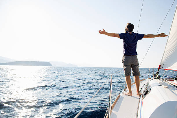 man stands at bow of yacht with arms outstretched - travel stock pictures, royalty-free photos & images
