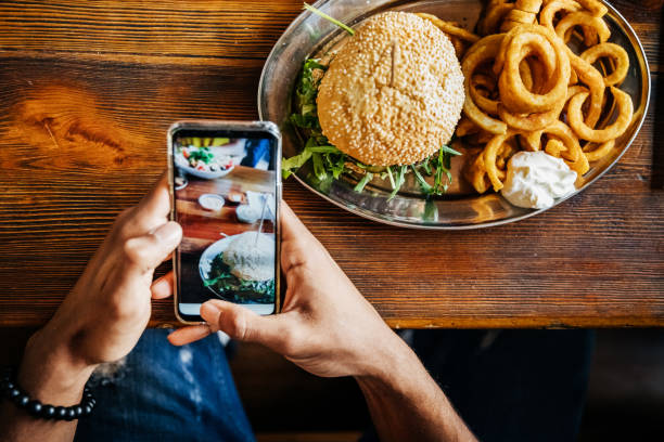 man talking picture of burger with smartphone - junk food stock pictures, royalty-free photos & images