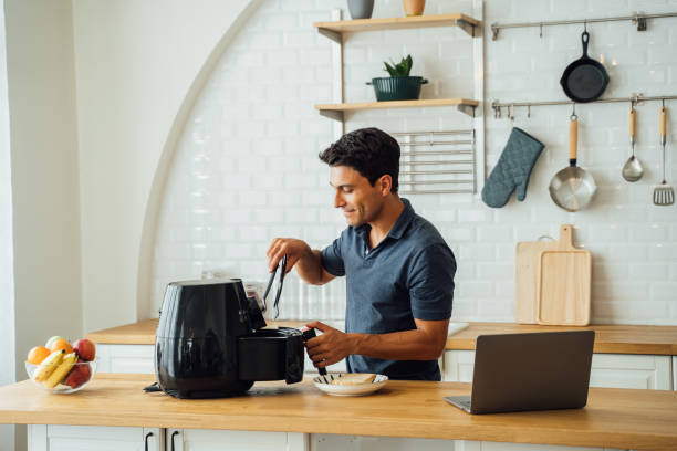 man using air fryer and laptop in kitchen - food stock pictures, royalty-free photos & images