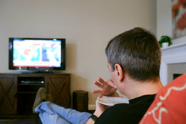 man watches tv while eating snack - junk food stock pictures, royalty-free photos & images