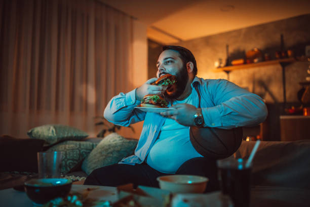 man watching a sports match and eating burger - junk food stock pictures, royalty-free photos & images