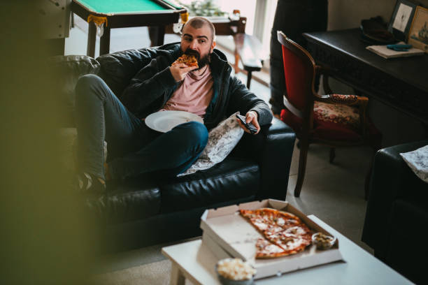 man watching tv and eating take-out pizza at home - junk food stock pictures, royalty-free photos & images
