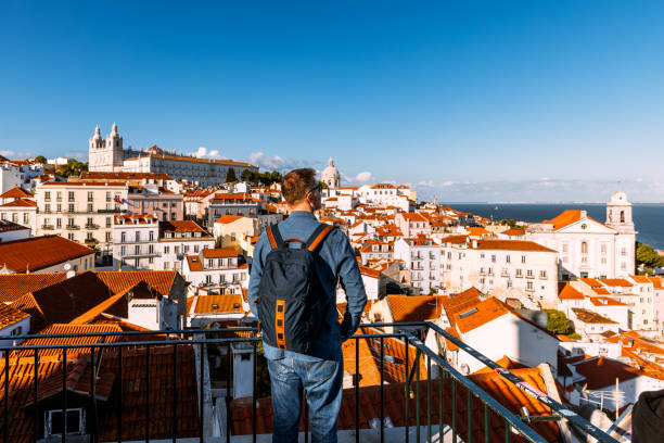 man with backpack looking at lisbon old town cityscape from a scenic viewpoint (miradouro), portugal - travel stock-fotos und bilder