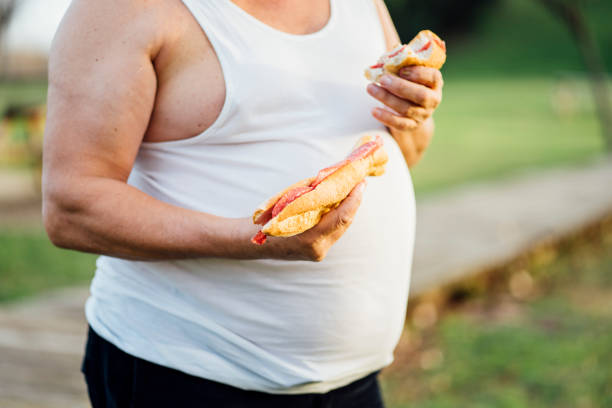 man with beer belly holding sandwich - junk food stock pictures, royalty-free photos & images