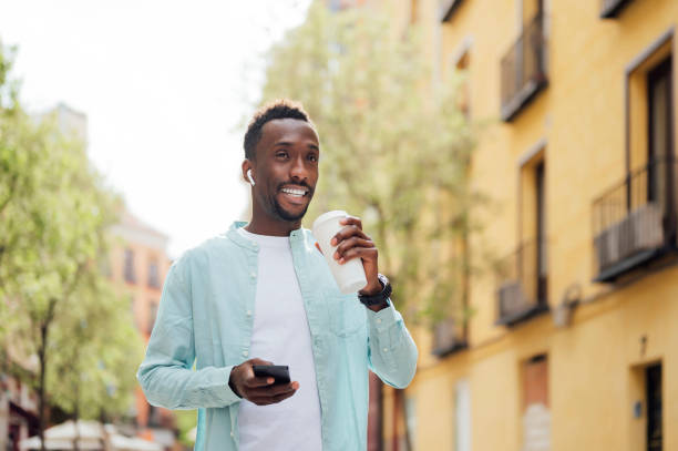 man with in-ear headphones holding reusable cup at street - junk food stock pictures, royalty-free photos & images