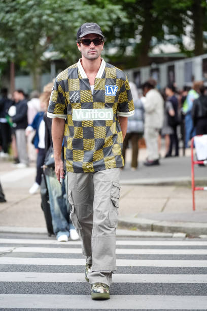 Marc Forne wears Nike baseball cap hat, Louis Vuitton sports jersey shirt with checkered pattern/print and Louis Vuitton patches, gray cargo pants,...