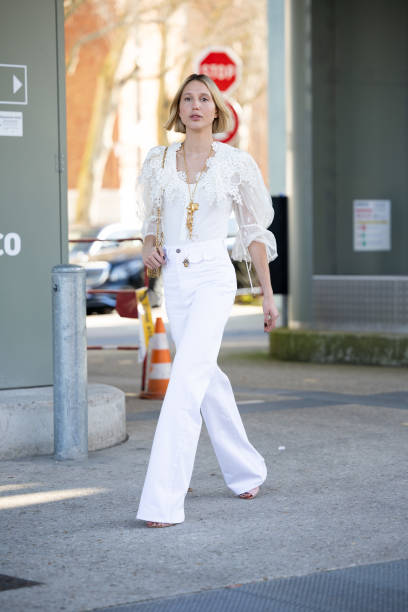 Maria Olympia of Greece and Denmark wears a gold necklace, a white lace puffy sleeves shirt, beige heels, white high waist flared trousers and a gold...