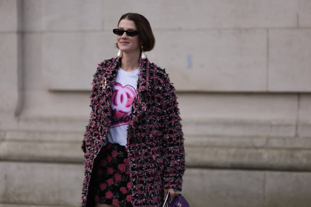 Marianne Theodorsen is seen wearing black sunglasses, long pearl earrings, a white t-shirt with the Chanel logo in pink, a long pink and black plaid...