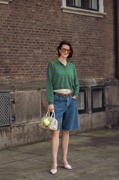 Marianne Theodorsen wears blue denim shorts, pink pointy shoes, green long sleeve shirt and orange sunglasses outside the Mark Kenly Domino Tan show...