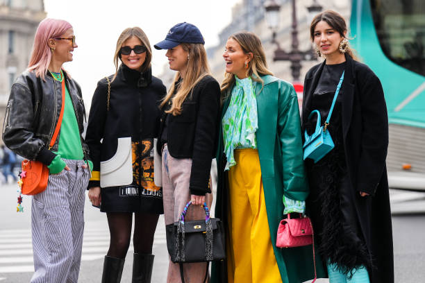Marianne Theodorsen wears orange sunglasses, gold and silver chain pendant necklace, a yellow and green pearls necklace, a blue t-shirt, a green wool...