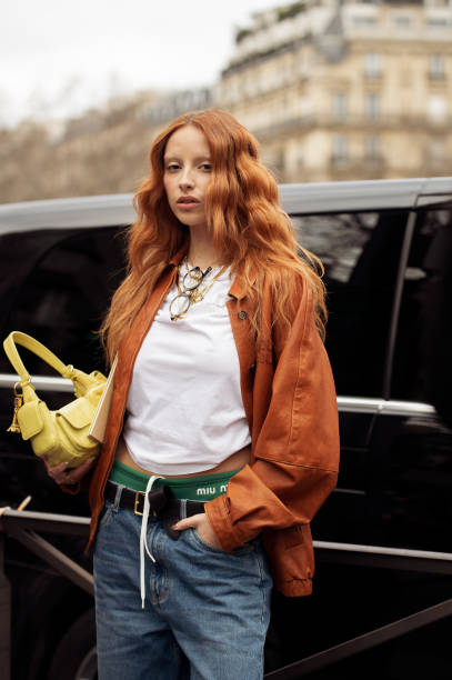Marie Gaguech wears jeans, green underwear, white top, orange jacket and yellow bag outside Miu Miu during the Womenswear Fall/Winter 2024/2025 as...