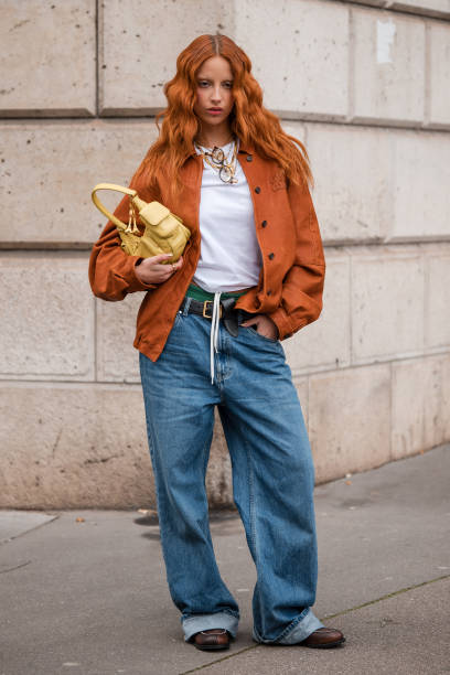 Marie Gaguech wears white tank top, orange shirt, blue jeans, yellow Miu Miu bag, brown loafers, outside Miu Miu, during the Womenswear Fall/Winter...