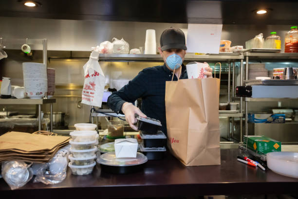 masked and gloved restaurant worker packaging food for delivery during covid-19 outbreak - junk food stock pictures, royalty-free photos & images