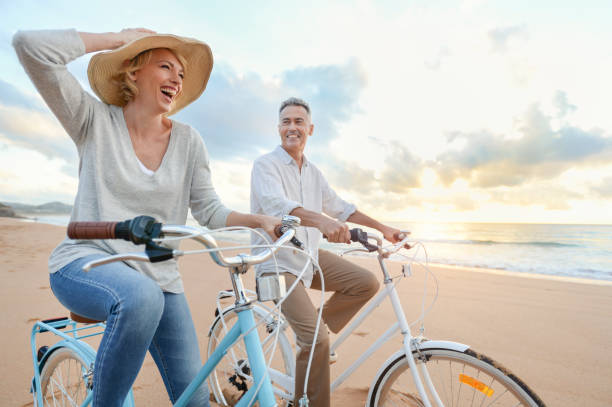 mature couple cycling on the beach at sunset or sunrise. - travel stock pictures, royalty-free photos & images