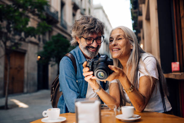 mature couple on vacation enjoying at the cafe and watching their photos - travel stock pictures, royalty-free photos & images