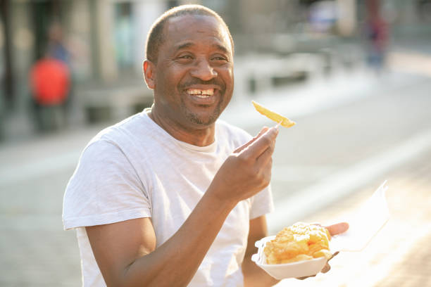 mature male eating fish and chips - junk food stock pictures, royalty-free photos & images