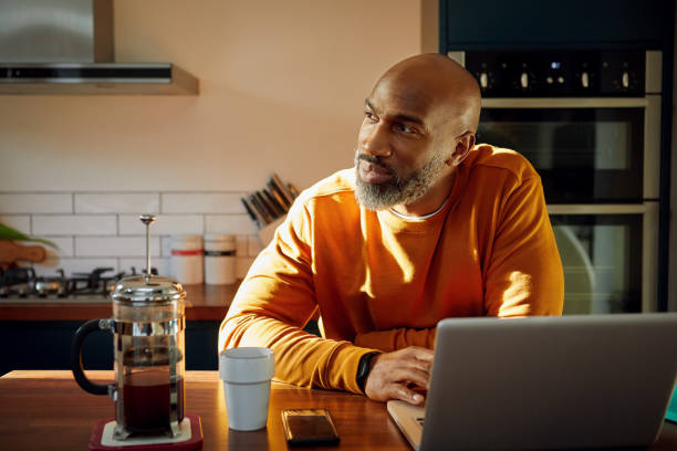mature man using laptop at kitchen island - home decoration photos et images de collection