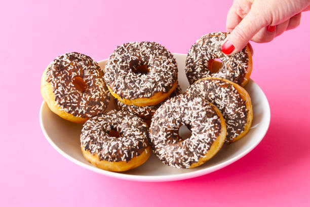 mature woman taking a doughnut - junk food stock pictures, royalty-free photos & images