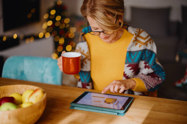 mature woman using digital tablet for online christmas shopping - home decoration stock pictures, royalty-free photos & images