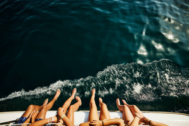 medium shot of teenagers feet hanging over side of sailboat - travel stockfoto's en -beelden