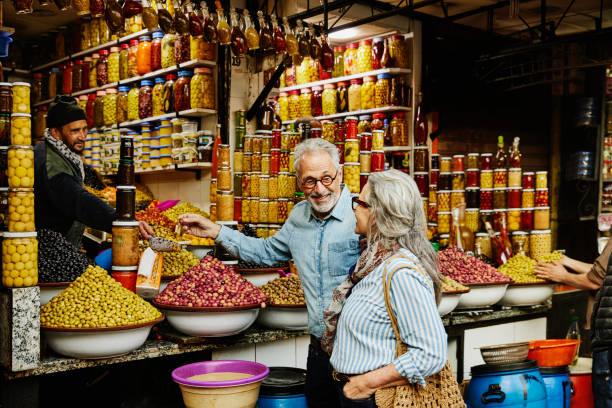 medium wide shot couple sampling olives in the medina of marrakech - travel stock pictures, royalty-free photos & images