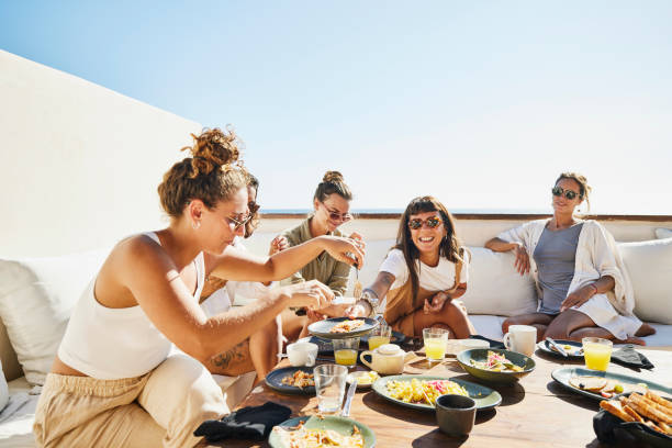 medium wide shot of smiling female friends sharing breakfast on deck of luxury suite at tropical resort - food stock pictures, royalty-free photos & images