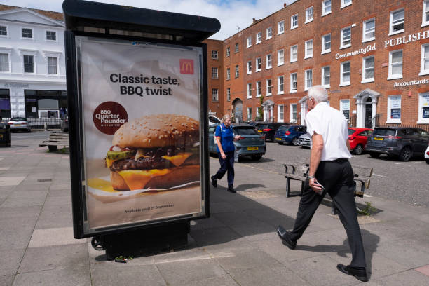 Members of the public pass a bus stop advertisement for McDonald's, the international fast food restaurant, and their new barbeque quarter pounder on...