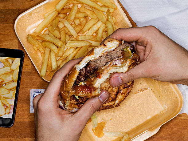 men eating hamburger and fries, phone with picture - junk food stock pictures, royalty-free photos & images