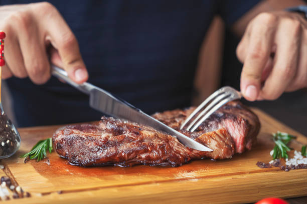 men's hands holding knife and fork, cutting grilled steak - food stock pictures, royalty-free photos & images