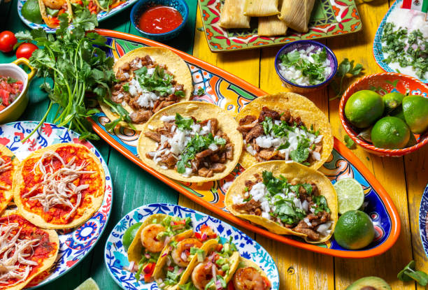 mexican independence day table, food for independencia -chiles en nogada, tacos al pastor, chalupas pozole, tamales, chicken with mole poblano sauce. yellow and green wooden background - food stock pictures, royalty-free phot
