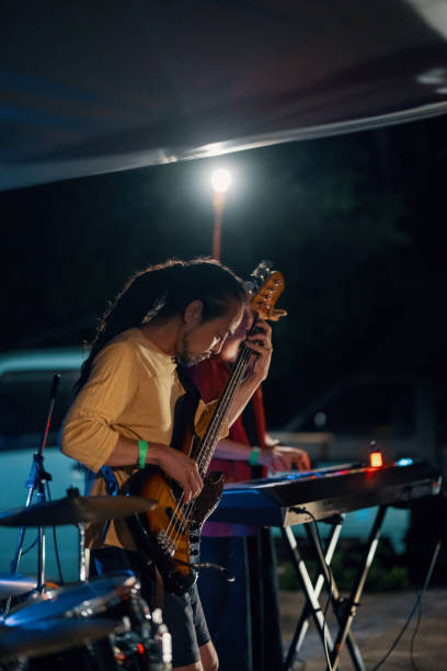 mid adult man playing a bass guitar in a band at an outdoor music festival - concert stock pictures, royalty-free photos & images