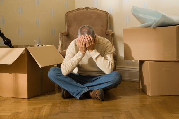 mid adult man sitting on a hardwood floor and suffering from a headache - home decoration stock pictures, royalty-free photos & images