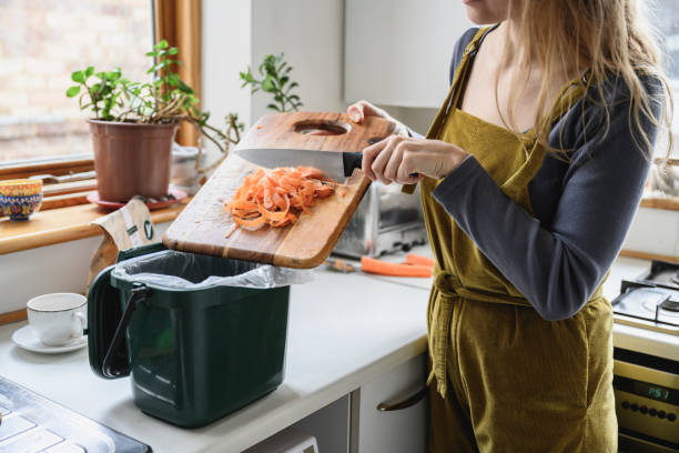 mid adult woman putting carrot shavings in compost bin - food stock pictures, royalty-free photos & images