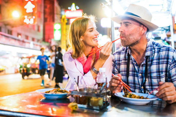 middle-aged man and his companion handsome blond lady in bangkok chinatown - food stock pictures, royalty-free photos & images