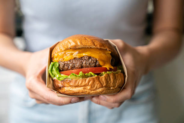 midsection of woman holding burger - junk food stock pictures, royalty-free photos & images