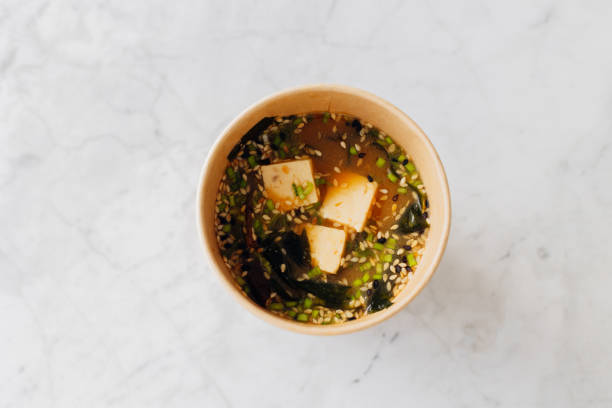 miso traditional japanese soup with tofu, mushrooms, spring onion and sesame seed mix in cardboard reusable glass. high angle view. - junk food stock pictures, royalty-free photos & images