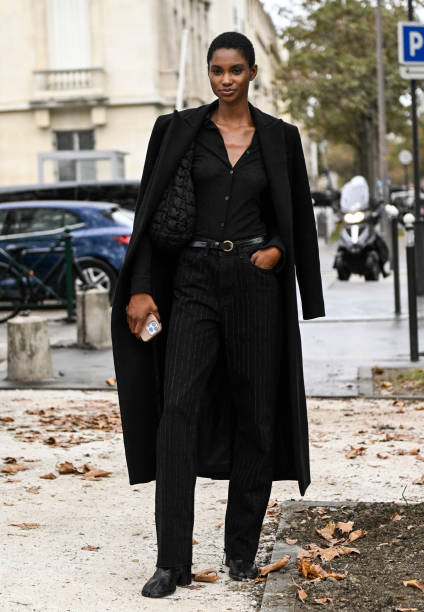 Model is seen wearing a black biker overcoat, black shirt, black striped pants and black belt with a black bag outside the Chanel show during the...