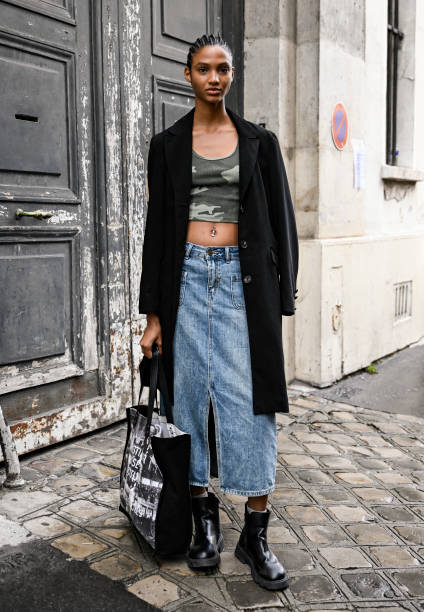 Model is seen wearing a black coat, camo crop top, blue slit denim skirt and black boots outside the Giambattista Valli show during Womenswear...