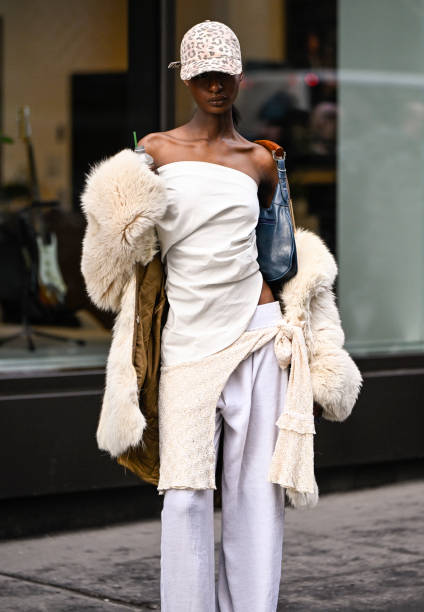 Model is seen wearing a cream fur coat, cream top and white pants, blue and tan bag, gold cuff and animal print hat outside the Lapointe show during...