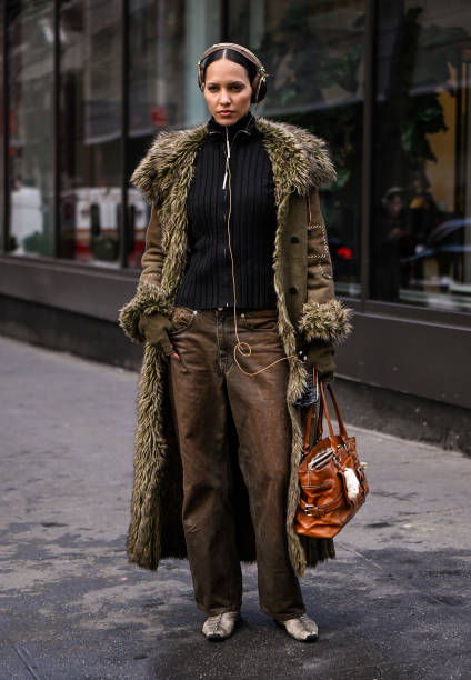 Model is seen wearing a green faux fur coat, black sweater, brown jeans and tan bag with brown headphones outside the Lapointe show during NYFW F/W...