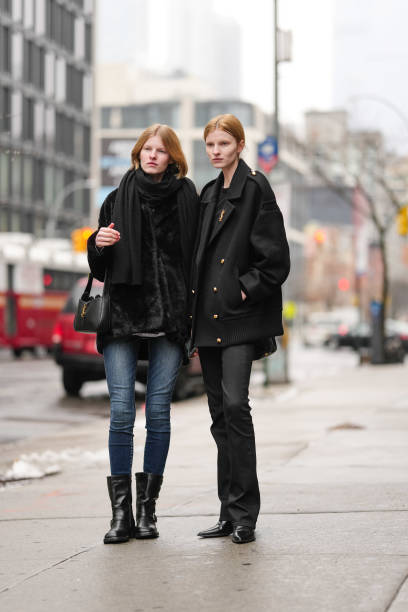 Model wears a black scarf, a black fluffy coat ; a model wears a black oversized jacket with a YSL brooch, outside Brandon Maxwell, during New York...