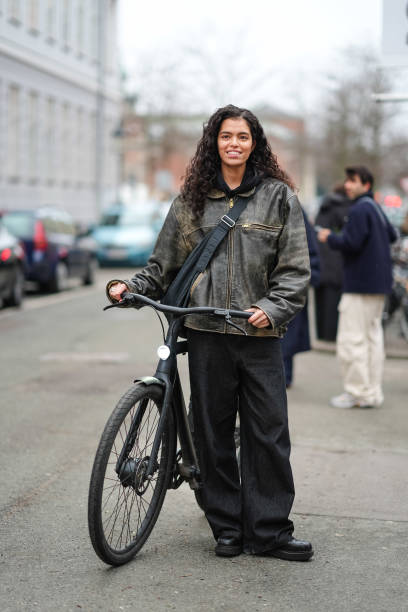 Model wears a leather jacket, crossbody bag, black flared pants , leather shoes , uses a bike / bicycle, outside Lovechild 1979, during the...