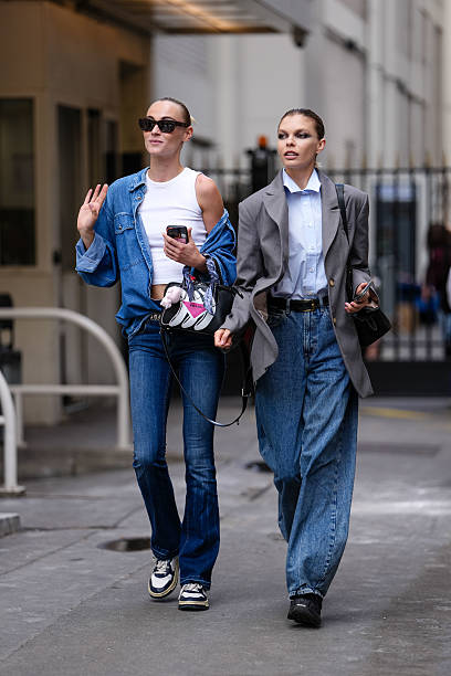 Model wears a white sleeveless crop top paired with a blue denim jacket. The jacket features a classic collar and button-down front. Blue denim jeans...