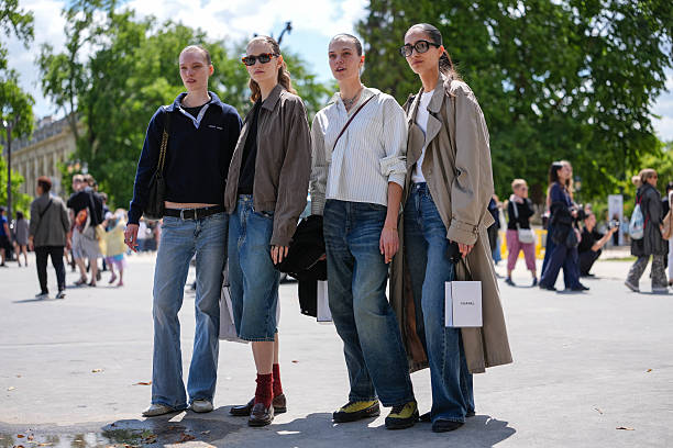 Model wears black t-shirt, navy blue long sleeve Miu Miu sweeter, shiny black leather bag, black leather belt, navy blue washed denim jean pants,...