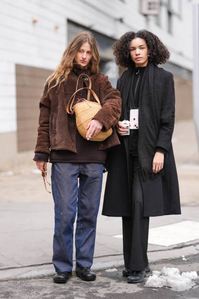 Model wears dark brown sunglasses, dark brown suede jacket, dark brown sweater, navy blue relaxed trouser pants, light brown woven basket, shiny...