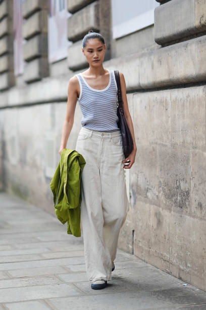 Model wears white and light blue striped tank top, white denim jean loose pants, bright green jacket in hand, dark brown leather bag, white boots...